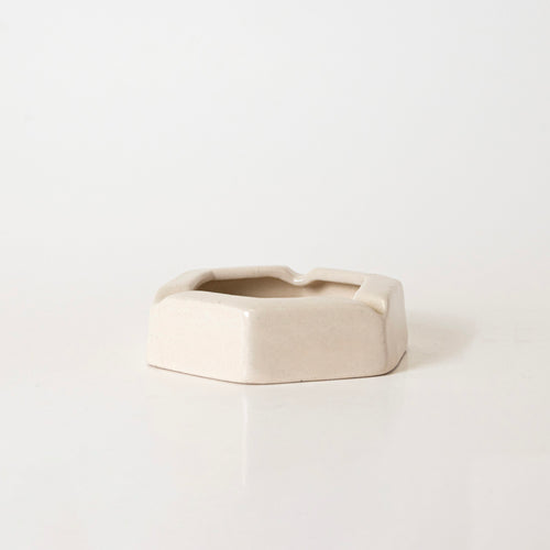 The kalakriti PENTAGON HORIZON is a beige ceramic ashtray with a hexagonal shape and three grooves, displayed on a plain white surface against a white background.